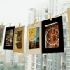 Paper picture frames with clips and photos hanging on a string, featuring a multi-story building in the background.