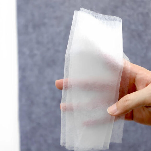 A close-up view of translucent iron-on pants hem tape held against the hand to show its texture and softness.