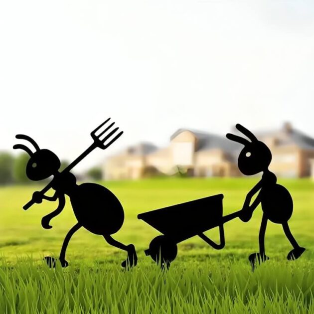 Metal ant garden decoration with pitchfork and wheelbarrow in front of a house on green grass.