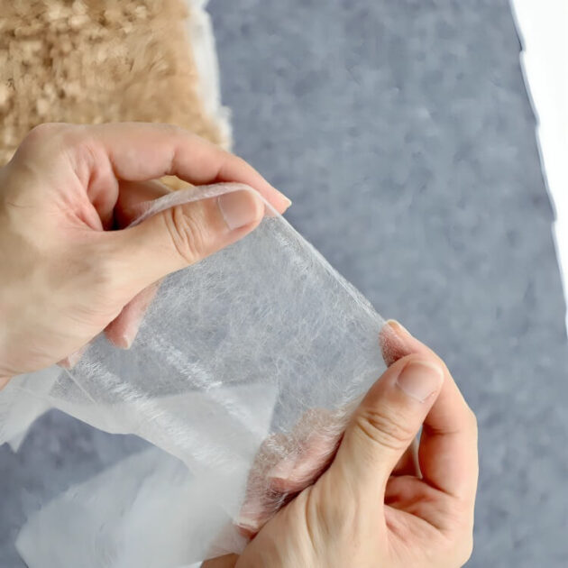 A woman is holding a piece of iron-on pants hem tape for no sew hemming and quick pant length adjustment.