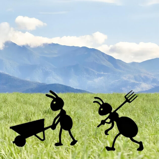 Two metal ant garden decorations on green grass with a scenic mountain view in the background.