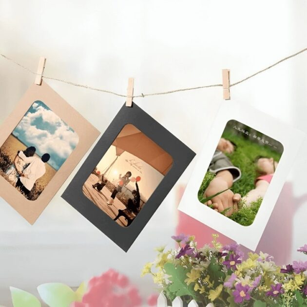 Paper photo frames in black, white, and brown with pictures hanging on a string, decorated with flowers in the background.